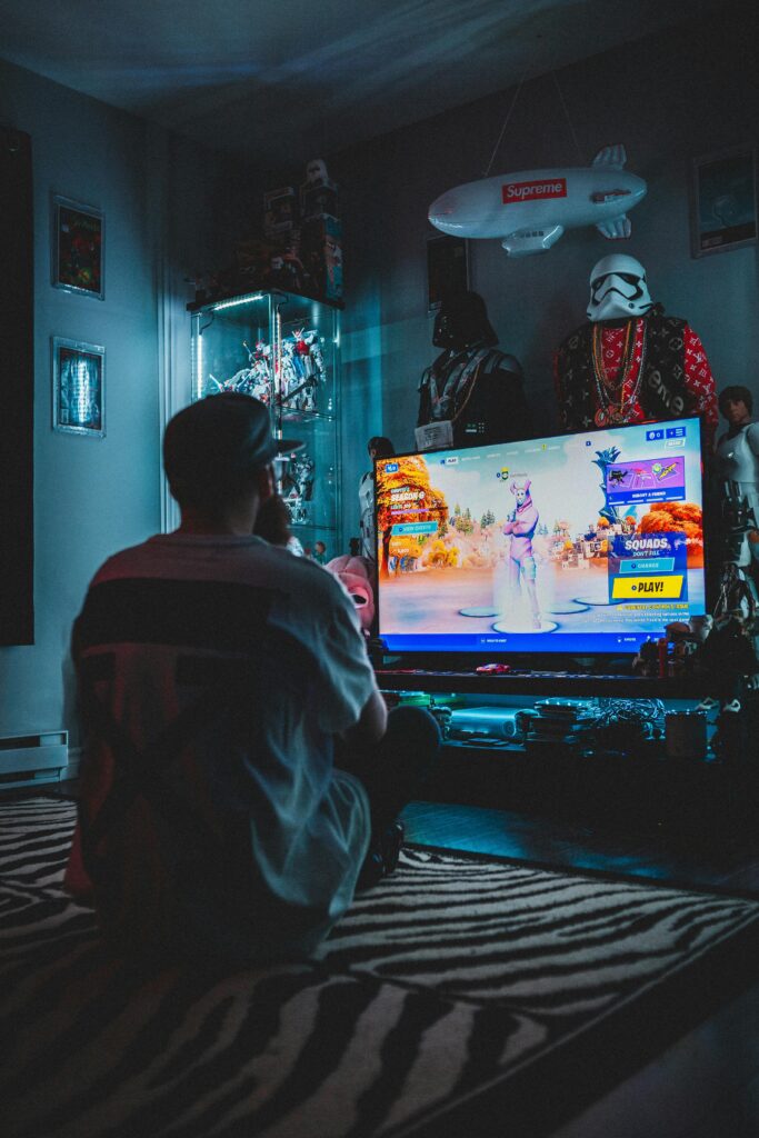Back view of anonymous male in casual wear sitting on floor and playing game on TV set in room full of things from movies