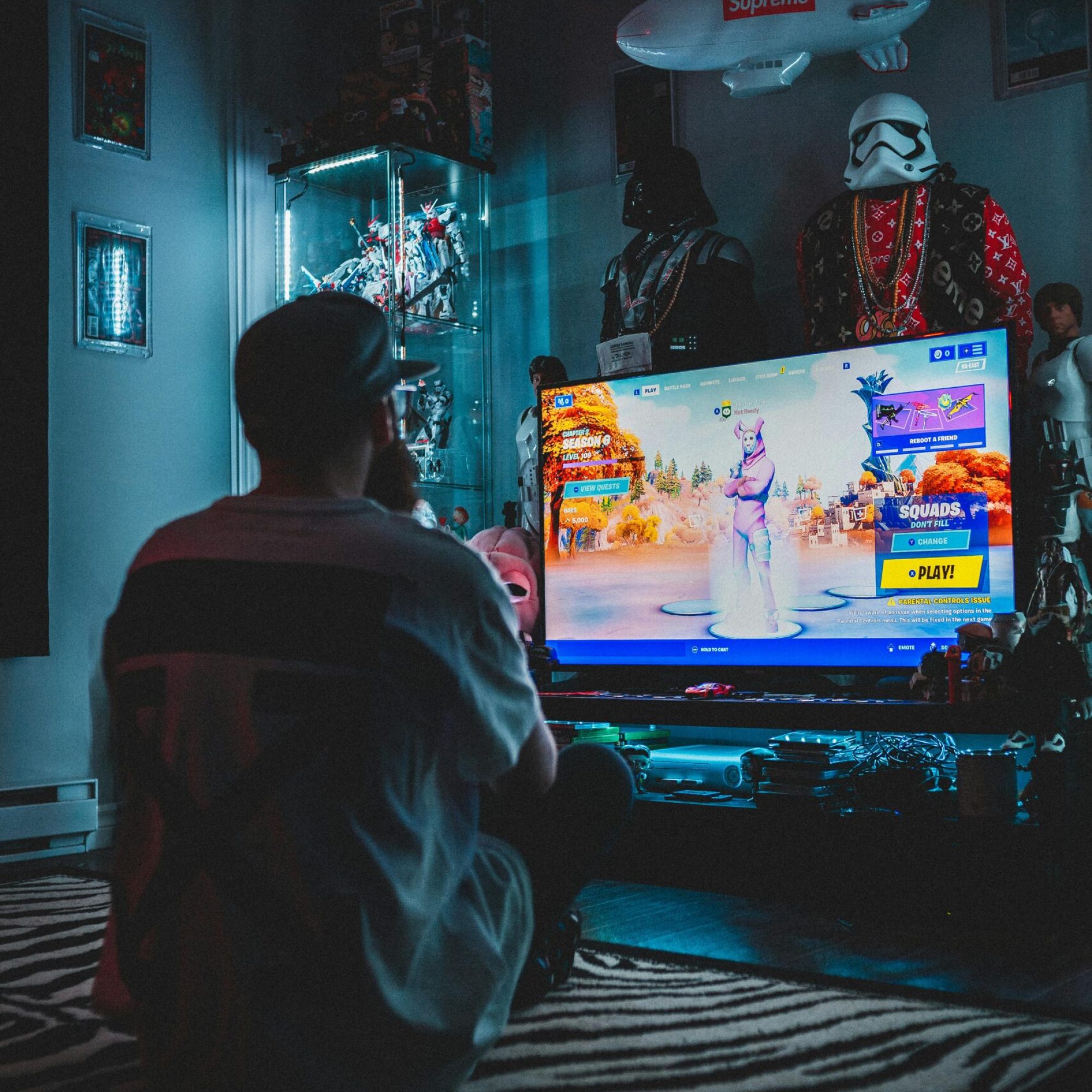 Back view of anonymous male in casual wear sitting on floor and playing game on TV set in room full of things from movies